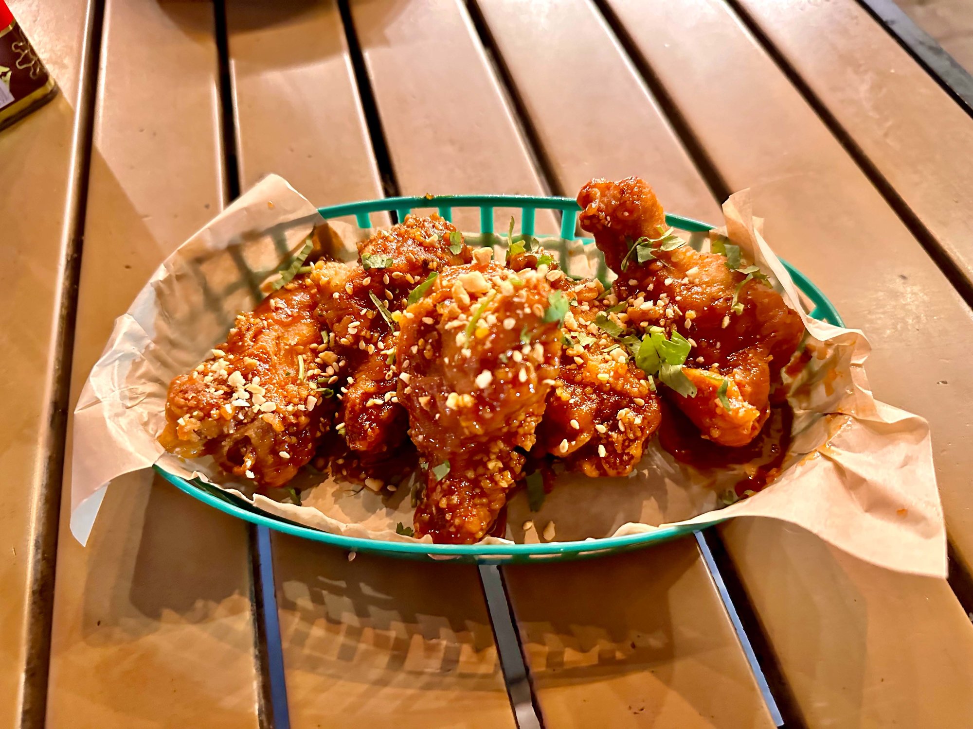 korean twice fried wings in a teal plastic container with paperon a table